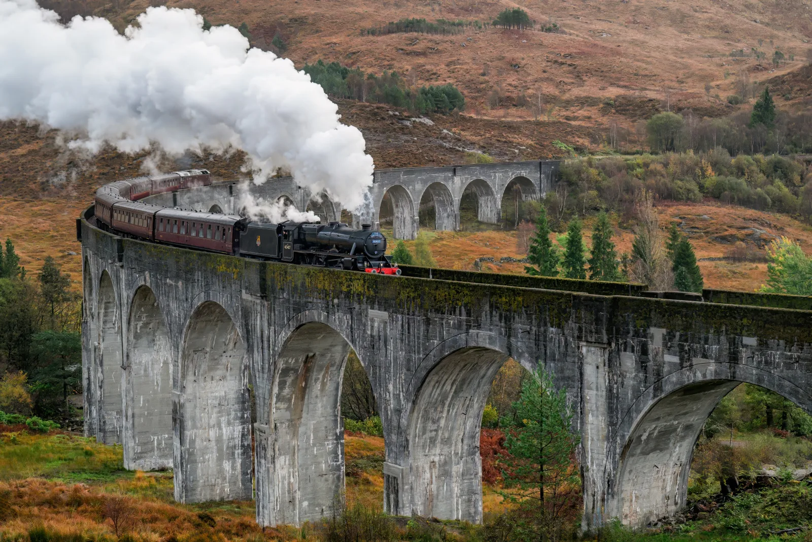 A train crossing a Highland viaduct surrounded by green hills